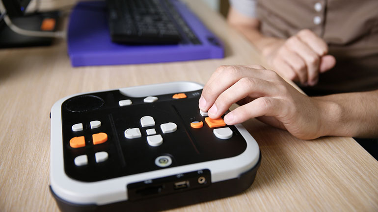 Blind person using a device for visually impaired, listening to audio book on his computer. Blindness aid, visual impairment, independent life concept.